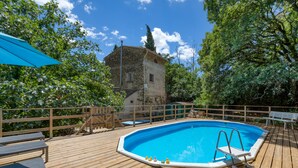 A wooden deck with a swimming pool, outdoor furniture, and a stone building in the background.