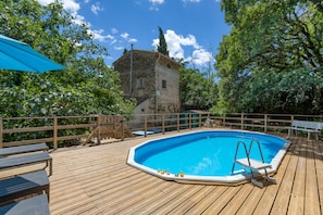 A wooden deck with a swimming pool, outdoor furniture, and a stone building in the background. - Eco-friendly Gîte with Private Pool, Terrace and Wi-Fi in Autignac (Autignac)