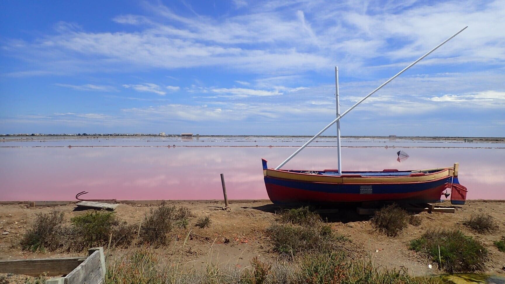 A boat on a beach with a calm body of water in the background.