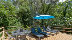 A wooden deck with a table and chairs, two lounge chairs, and a blue umbrella.