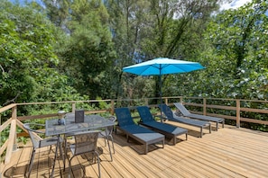A wooden deck with a table and chairs, two lounge chairs, and a blue umbrella. - Eco-friendly Gîte with Private Pool, Terrace and Wi-Fi in Autignac (Autignac)
