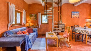 A cozy room with a sofa, a dining table, and a chair. There is a window with curtains, a lamp, and a painting on the wall.