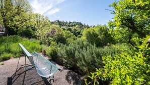 A bench in a garden with dense greenery and trees in the background.