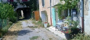 Une cour avec un chemin de gravier, une petite table et des chaises, des plantes en pot et un bâtiment doté d’une porte verte.