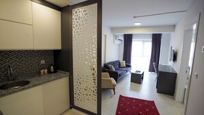 Uma cozinha moderna com pia, divisória decorativa e área de jantar com sofá e televisão.