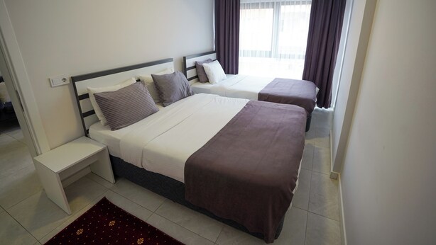 Quarto de hotel com duas camas, uma mesa de cabeceira, uma mesinha e vista para o exterior através de uma janela com cortinas.