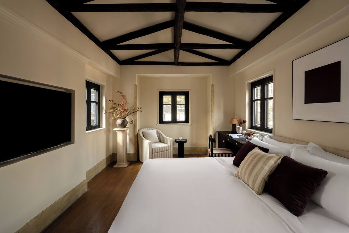 Una habitación de hotel con una cama grande, una silla, una mesita y un ventanal.