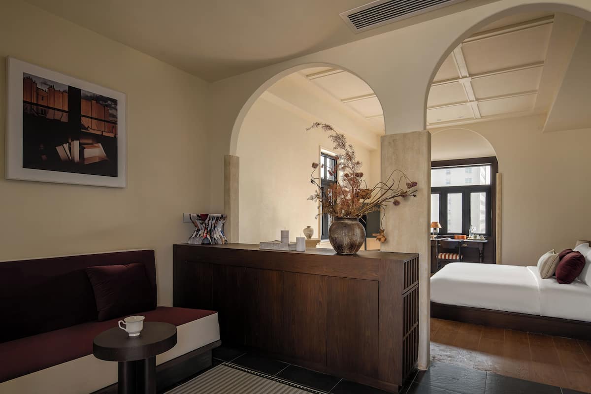 Habitación de hotel con sofá, una mesita, cama, escritorio y un jarrón con flores secas.