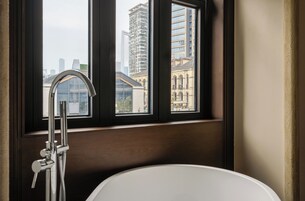 Un baño con bañera, ventana con vistas a edificios y un grifo moderno.