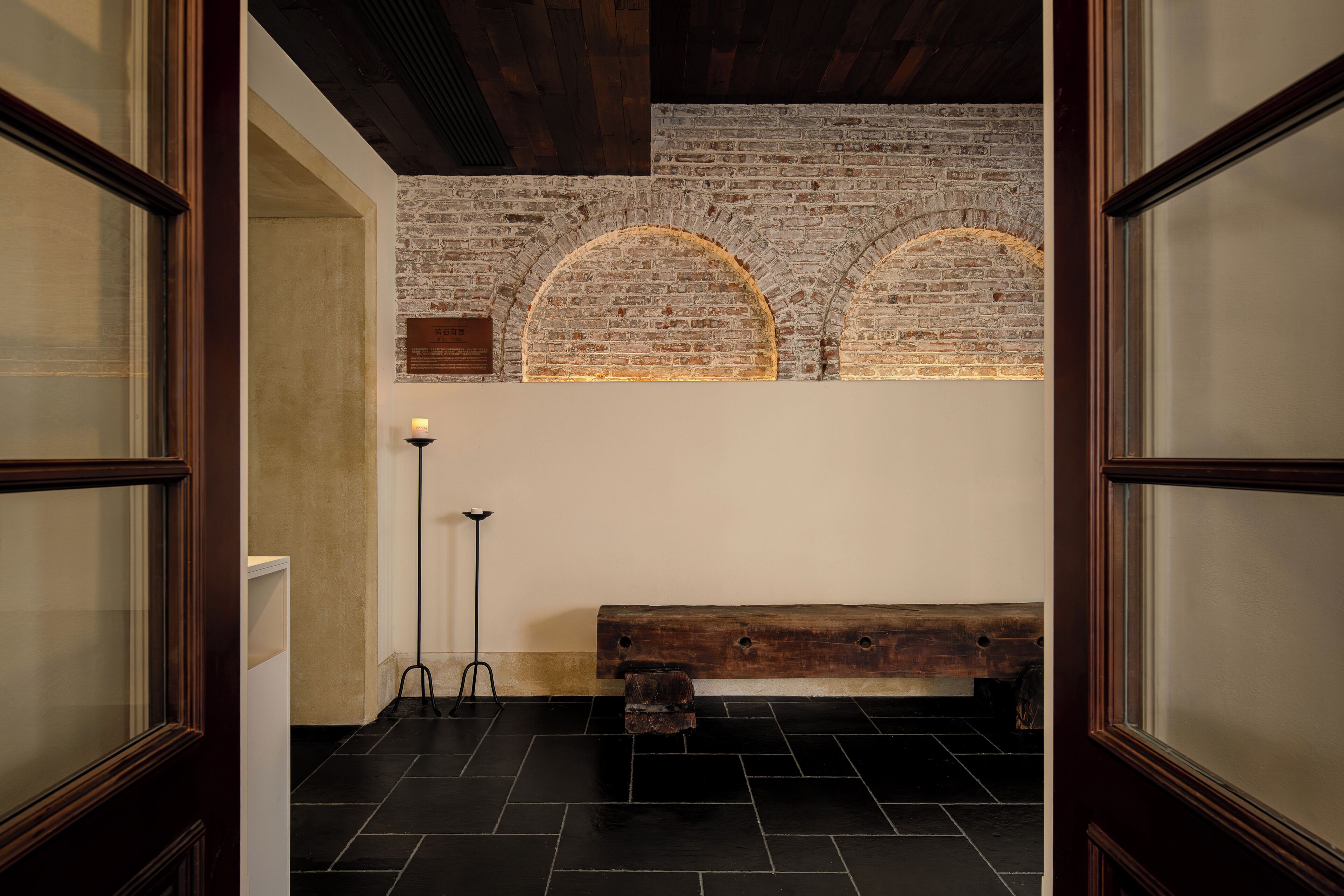 A room with a wooden bench, a brick wall, and a floor lamp.