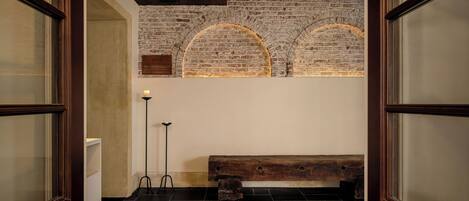 A room with a wooden bench, a brick wall, and a floor lamp.