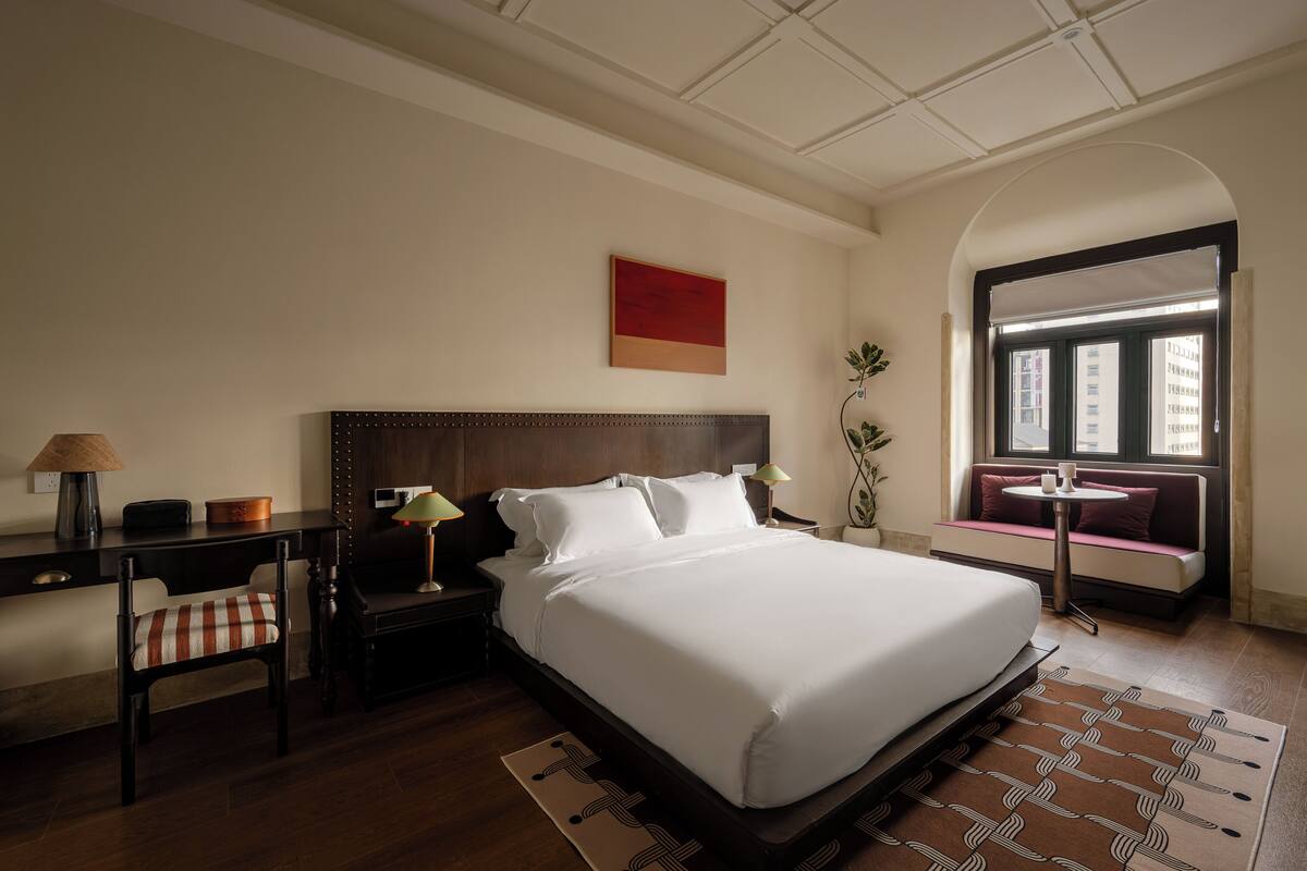 Habitación de hotel con una cama grande, un escritorio con silla, una mesita y una ventana con vistas.