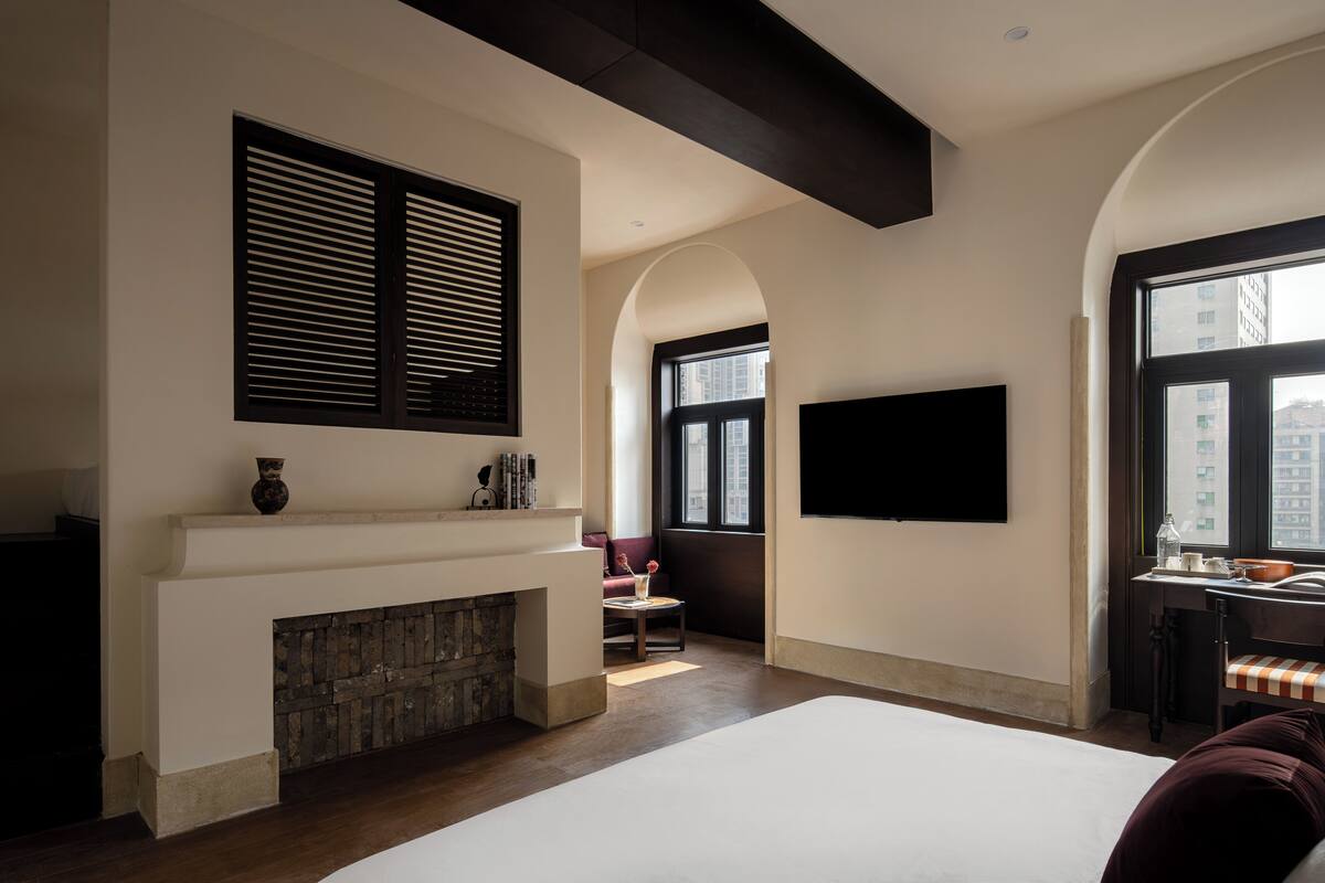 Un dormitorio con chimenea, una cama grande, un televisor en la pared y vistas de la ciudad a través de la ventana.