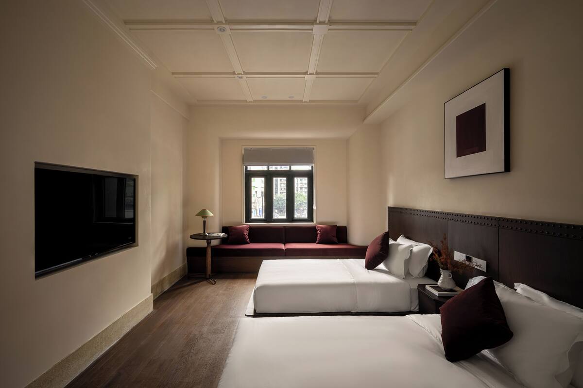 Habitación de hotel con una cama grande, una cama más pequeña, un sofá, un televisor, una ventana y un cuadro en la pared.
