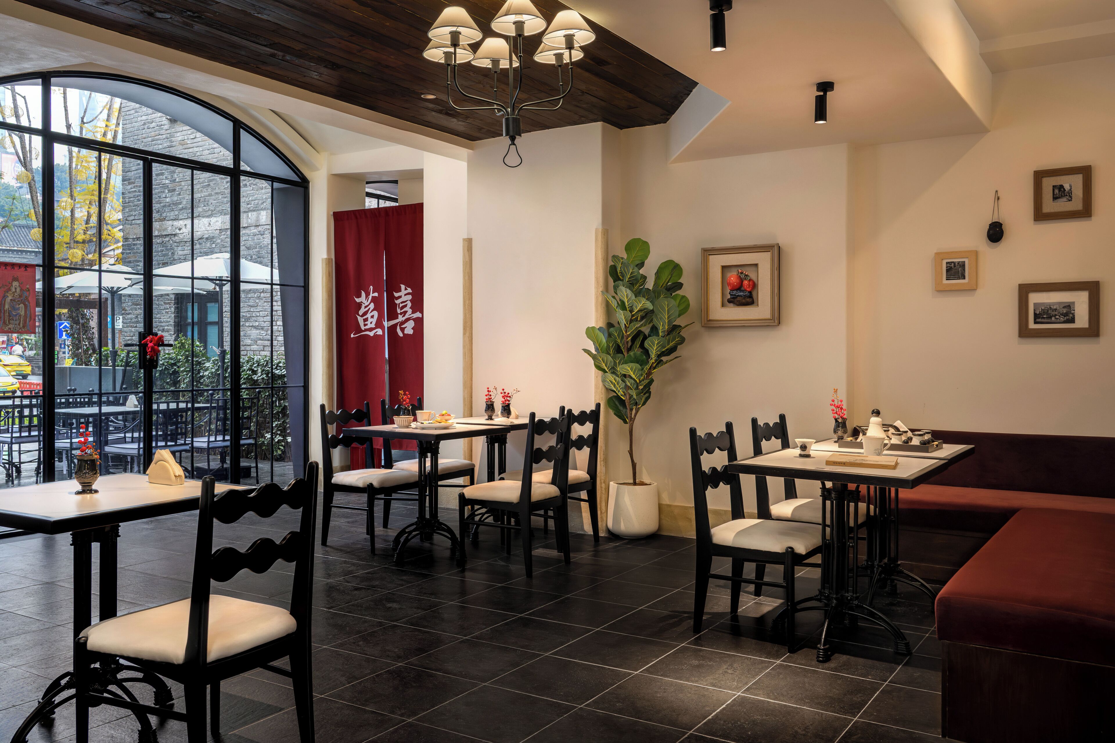 Ein Restaurantinneres mit Tischen, Stühlen, einem großen Fenster, einer Pflanze und gerahmten Bildern an der Wand.