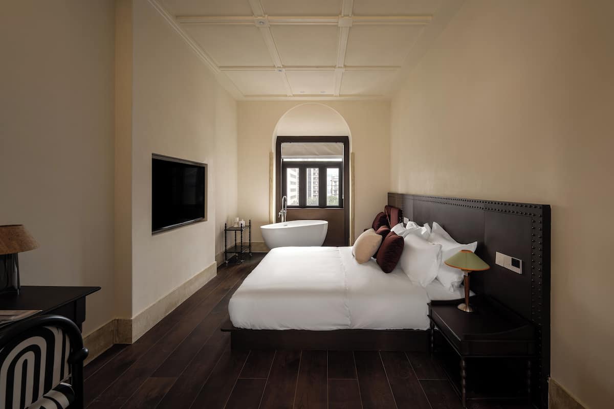 Un dormitorio con una cama grande, un televisor montado en la pared, una bañera y un ventanal de arco.