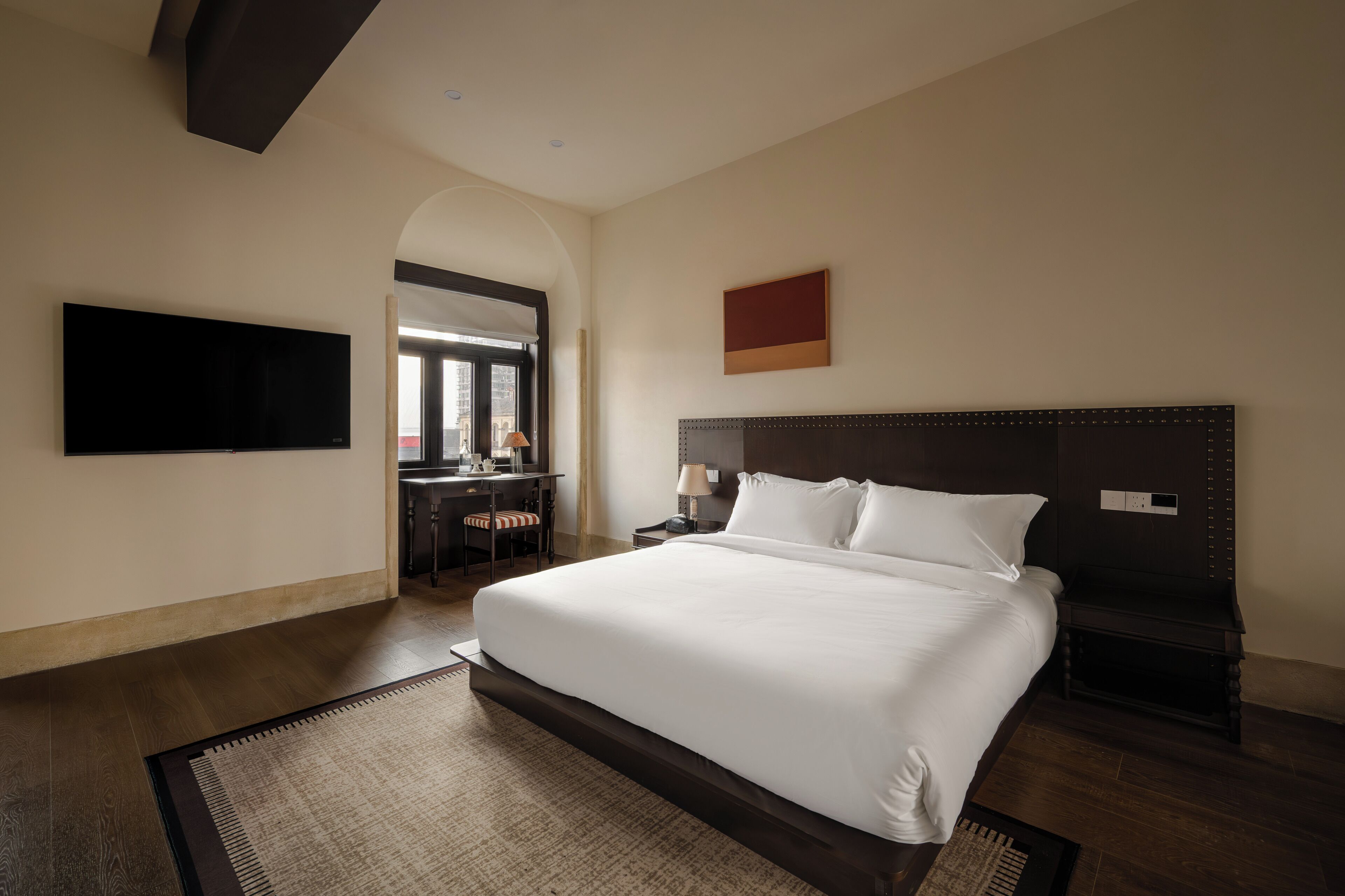 Una habitación de hotel con una cama grande, un escritorio con silla, un televisor de pantalla plana y un cuadro en la pared.