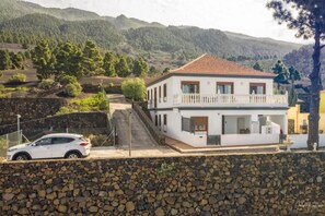 Una casa blanca de dos pisos con techo de tejas rojas, un balcón y un muro de piedra al frente.