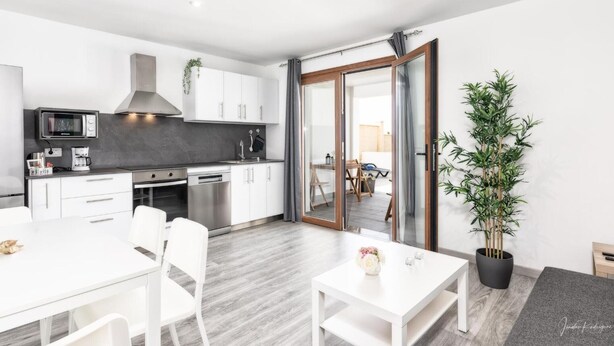 A modern kitchen with white cabinets, a microwave, and a stove. There is a dining area with a white table and chairs. - Apartment 'Cerca Nueva B1' with Sea View, Wi-Fi and Air Conditioning (El Paraíso)