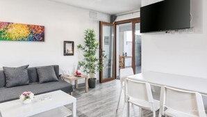 A modern living room with a sofa, a coffee table, a dining table with chairs, a potted plant, a television, and a colorful abstract painting. - Apartment 'Cerca Nueva B1' with Sea View, Wi-Fi and Air Conditioning (El Paraíso)