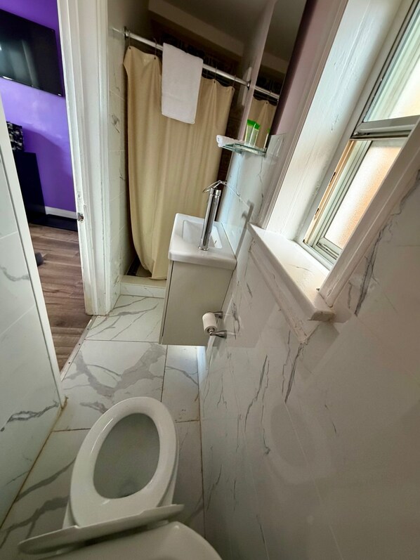 A bathroom with a toilet, sink, and shower area. - OSHAWA INN MOTEL (Oshawa)
