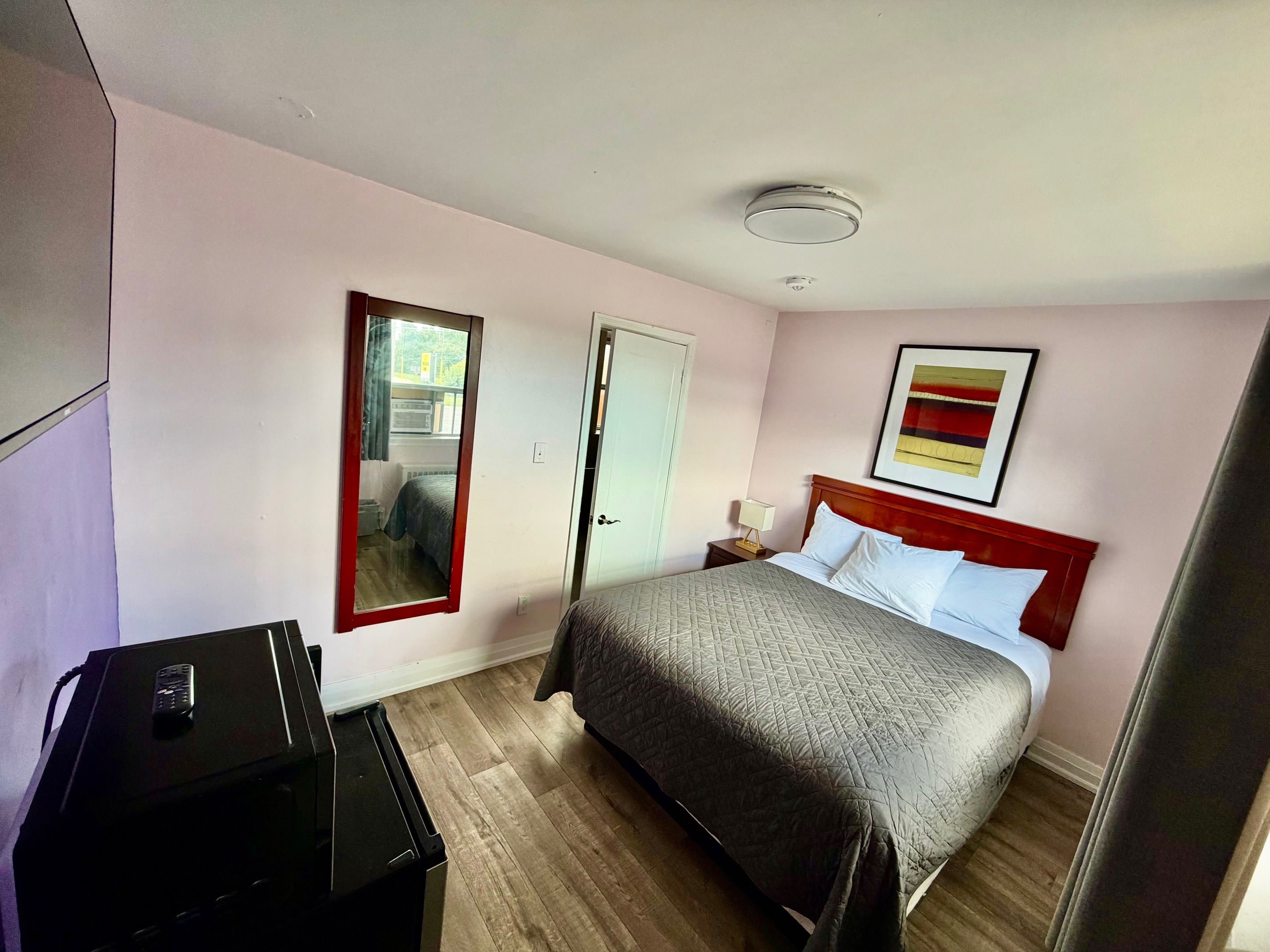 Une chambre d’hôtel avec un lit, une table de chevet avec une lampe, un miroir et un luminaire au plafond.