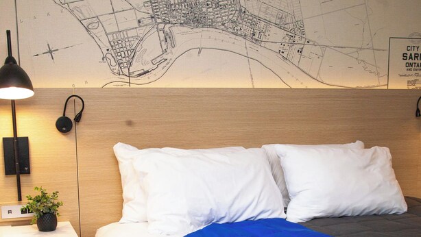 Habitación de hotel con cama, mesita de noche, lámpara, un mapa en la pared y una planta pequeña.
