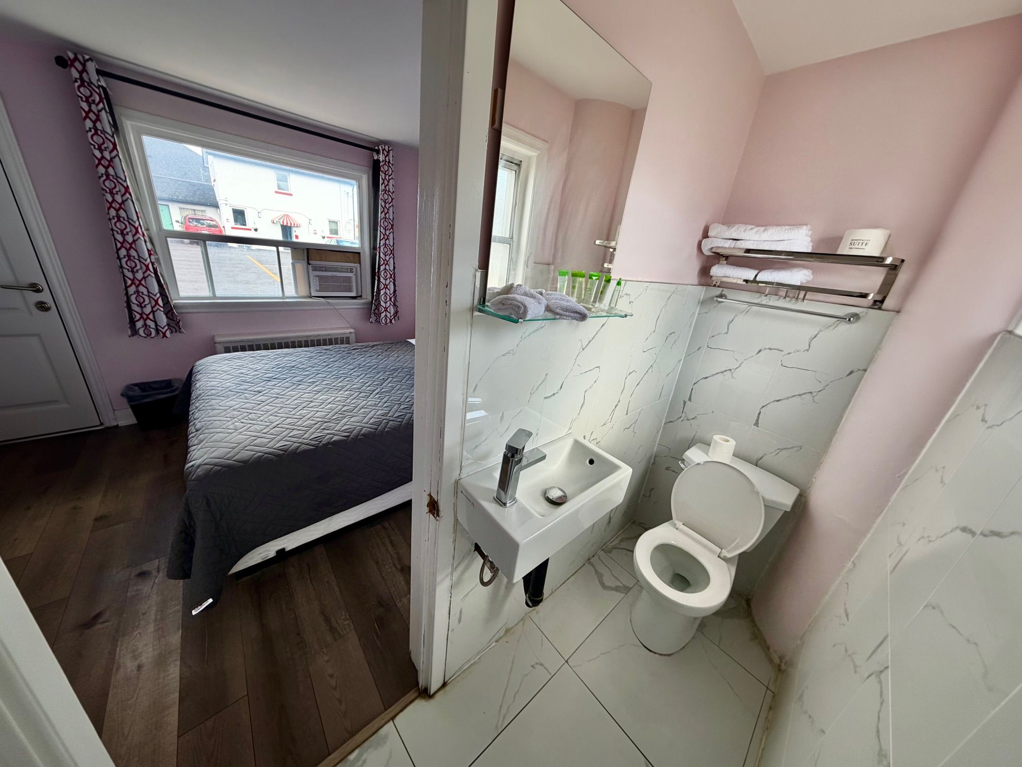 A compact bedroom with a bed, a window, and a bathroom with a toilet and sink.