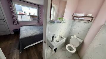 A compact bedroom with a bed, a window, and a bathroom with a toilet and sink.