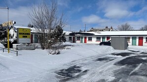 Un motel con un letrero que dice Oshawa Inn, un estacionamiento cubierto de nieve y un edificio con puertas rojas y verdes.