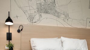 Un dormitorio con cama, una mesita de noche con lámpara, un mapa en la pared y una planta pequeña.