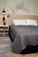 A bedroom with a bed, a nightstand with a lamp, a map on the wall, and a small plant.