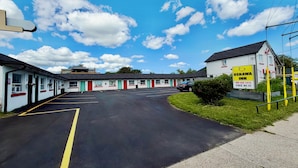 A motel with a parking lot, a building with a sign for Oshawa Inn, and a clear blue sky with clouds. - OSHAWA INN MOTEL (Oshawa)