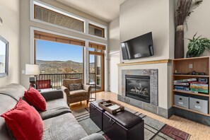 A spacious living room with a fireplace, a flat-screen TV, a sofa, a chair, and a bookshelf.