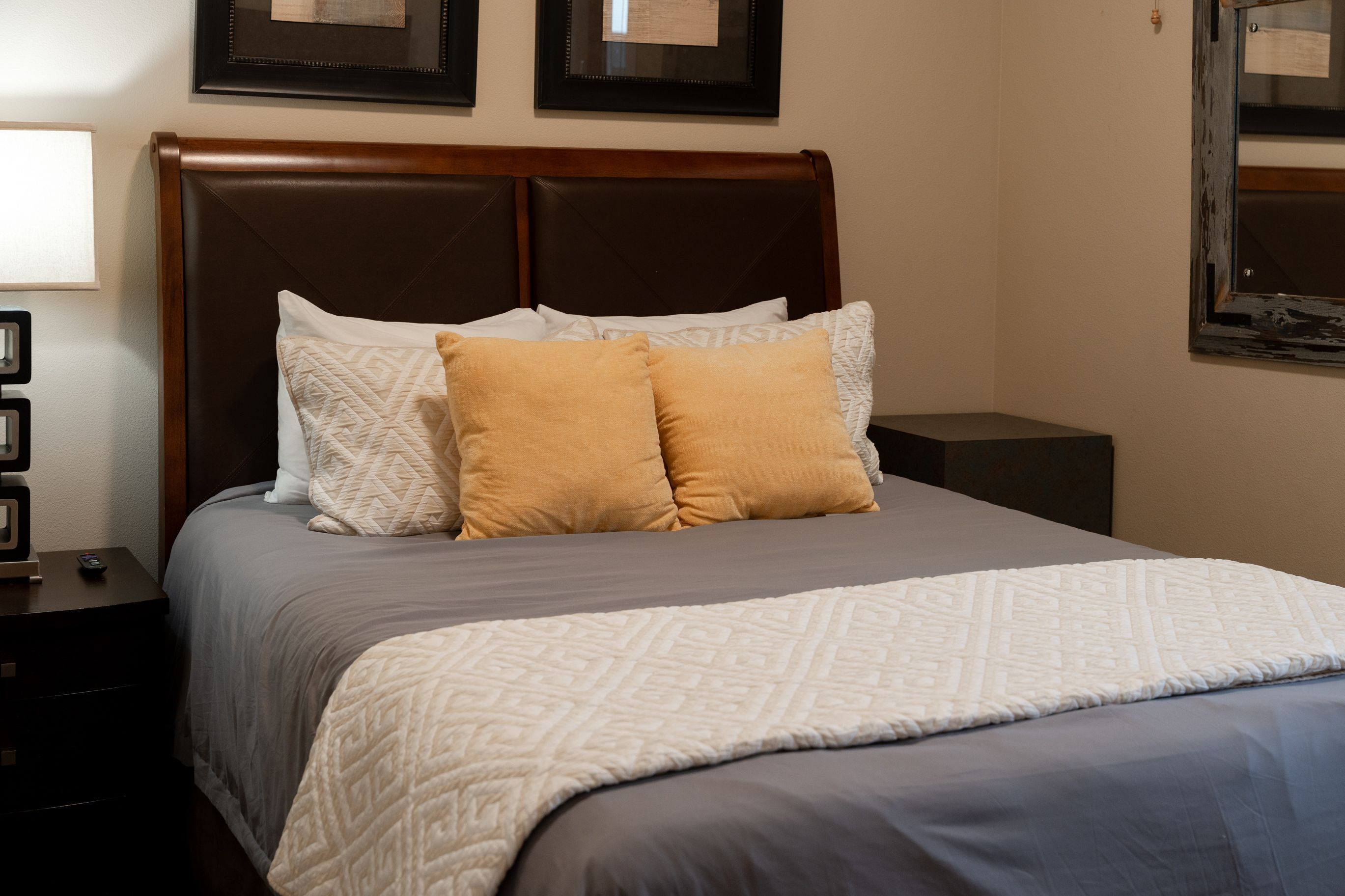 Cama bem arrumada com colcha estampada e duas almofadas, mesa de cabeceira com abajur e quadro na parede.