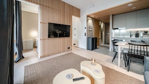 Ein modernes Wohnzimmer mit Fernseher, Essbereich und Küche.
