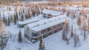 Ein modernes, mehrgeschossiges Gebäude mit flachem Dach, umgeben von einem dichten Wald mit schneebedeckten Bäumen.