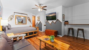 Une pièce comprenant un lit, une table basse en bois, un canapé, un ventilateur de plafond et un tableau accroché au mur.
