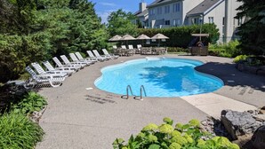 A swimming pool with lounge chairs and umbrellas, surrounded by greenery and a building in the background. - Modern Escape - Steps to Village + Summer Pool (The Blue Mountains)