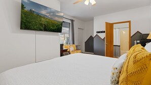 Ein Schlafzimmer mit einem Bett, einem an der Wand montierten Fernseher, einem Deckenventilator und einer Tür zu einem anderen Raum.