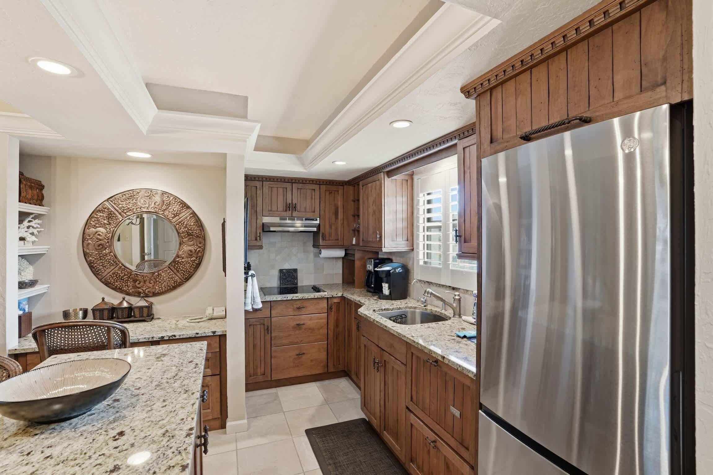 A kitchen with wooden cabinets, a stainless steel refrigerator, a round mirror, and a granite countertop.