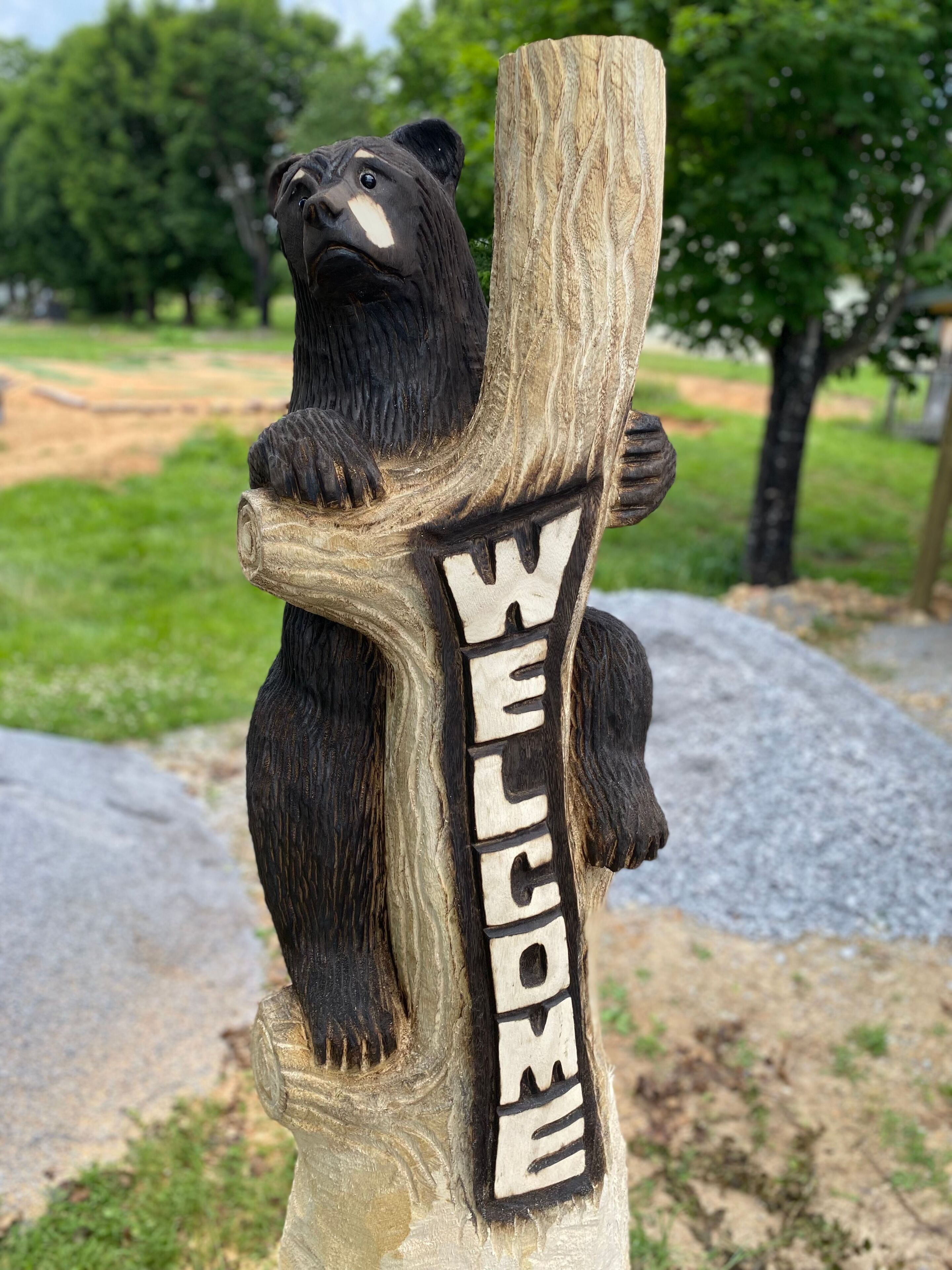 A wooden bear sculpture with a 'WELCOME' sign on a post.