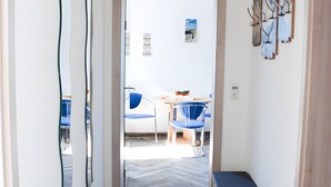 Un couloir mène à un espace repas comprenant une table et des chaises, une plante en pot et un luminaire fixé au mur.