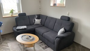 Un salon moderne avec un canapé d’angle gris foncé, une table basse ronde et une petite plante en pot près de la fenêtre.