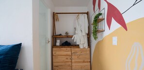 Ein kleines Zimmer mit einem Holzschrank, einem Kleiderhaken und einem an der Wand befestigten Regal mit einer Pflanze.