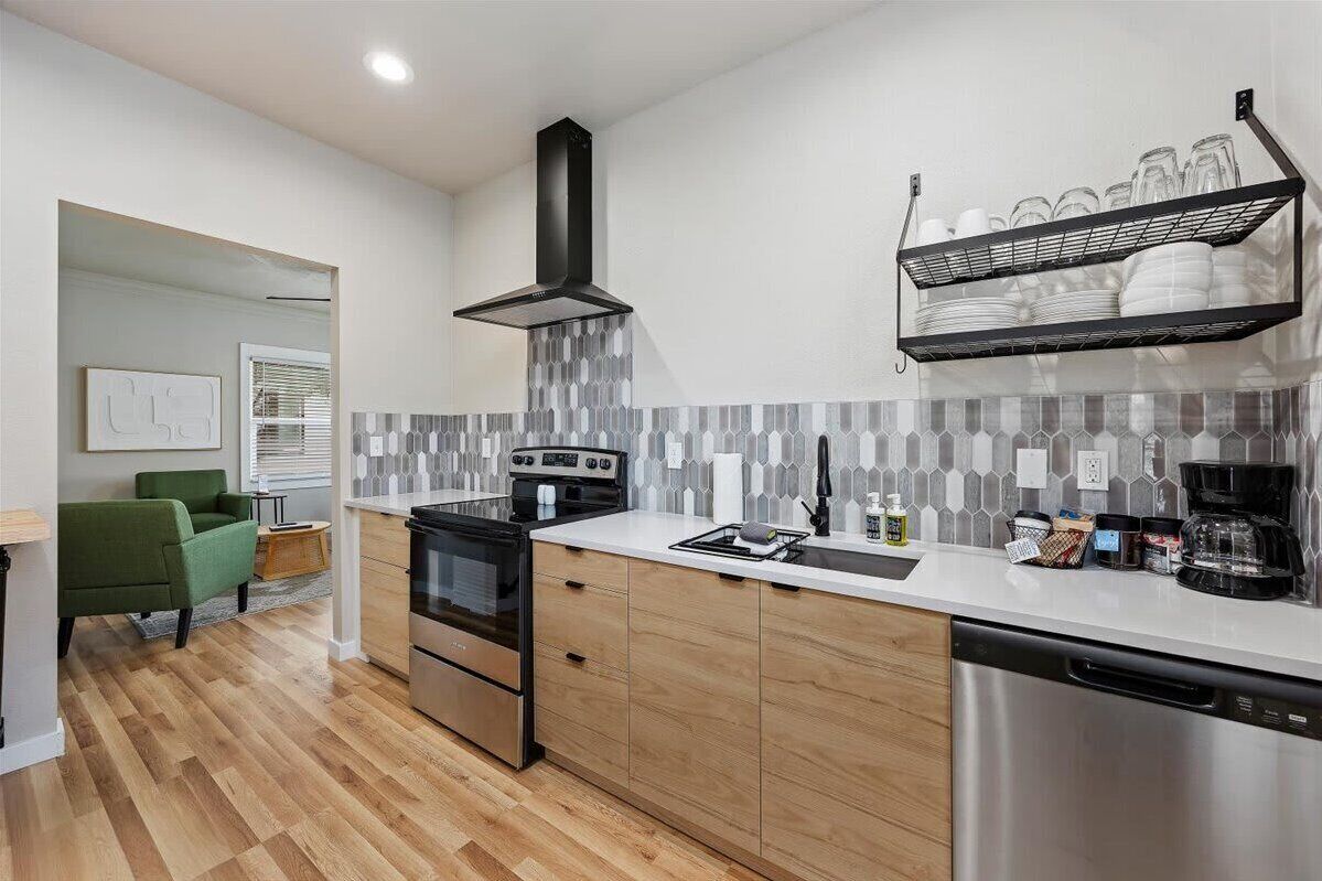 A modern kitchen with a stove, oven, dishwasher, and a black range hood.