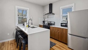 Una cocina moderna con una isla central, armarios blancos, extractor de aire negro y refrigerador de acero inoxidable.