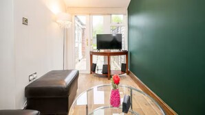 Un soggiorno con un tavolino in vetro, un divano in pelle nera, una televisione su un mobile in legno e una parete verde.