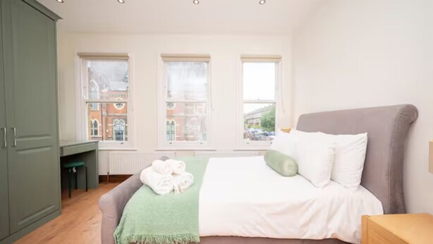 Una camera da letto con un letto, una scrivania e vista sugli edifici attraverso le finestre.