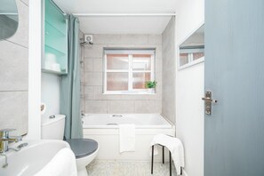 Ein Badezimmer mit Badewanne, Toilette, Waschbecken und einem Fenster mit Pflanze.